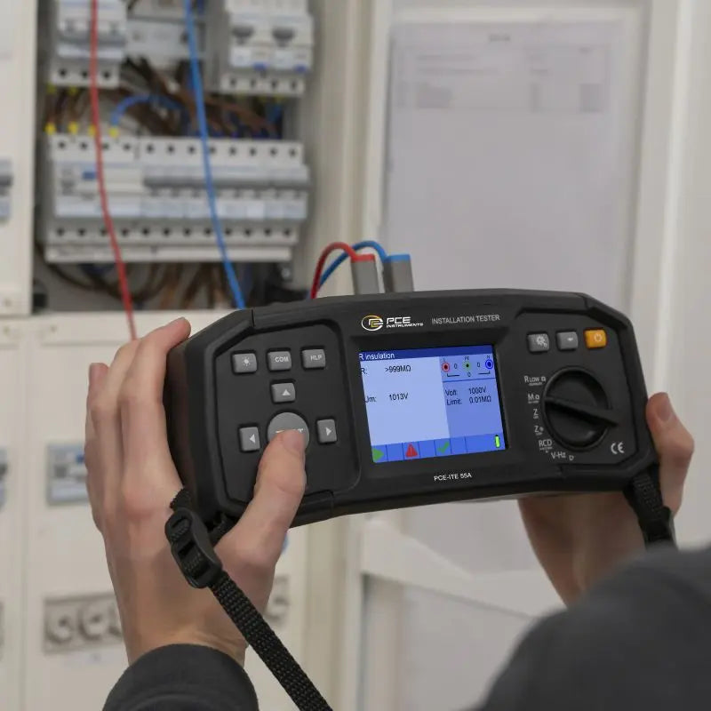 Μετρητής μόνωσης PCE Instruments PCE-ITE 55A σε χρήση μπροστά σε ηλεκτρικό πίνακα, με έγχρωμη οθόνη και επιλογέα λειτουργιών